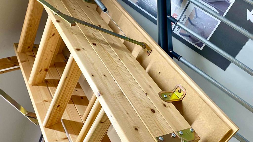 Seitenansicht auf eine zusammengeschobene Holz-Bodentreppe im Test, die an einer Decke im Verkaufsbereich ausgestellt ist.