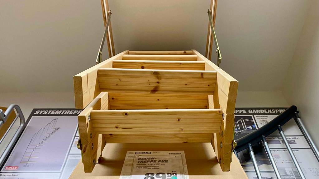 Ansicht von unten auf eine zusammengeschobene Holz-Bodentreppe im Test, die in einem Verkaufsbereich hängend ausgestellt ist.