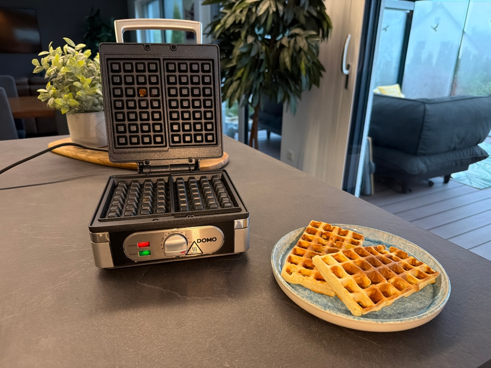 Zwei Waffeln liegen neben dem geöffneten Domo-Waffelautomat.
