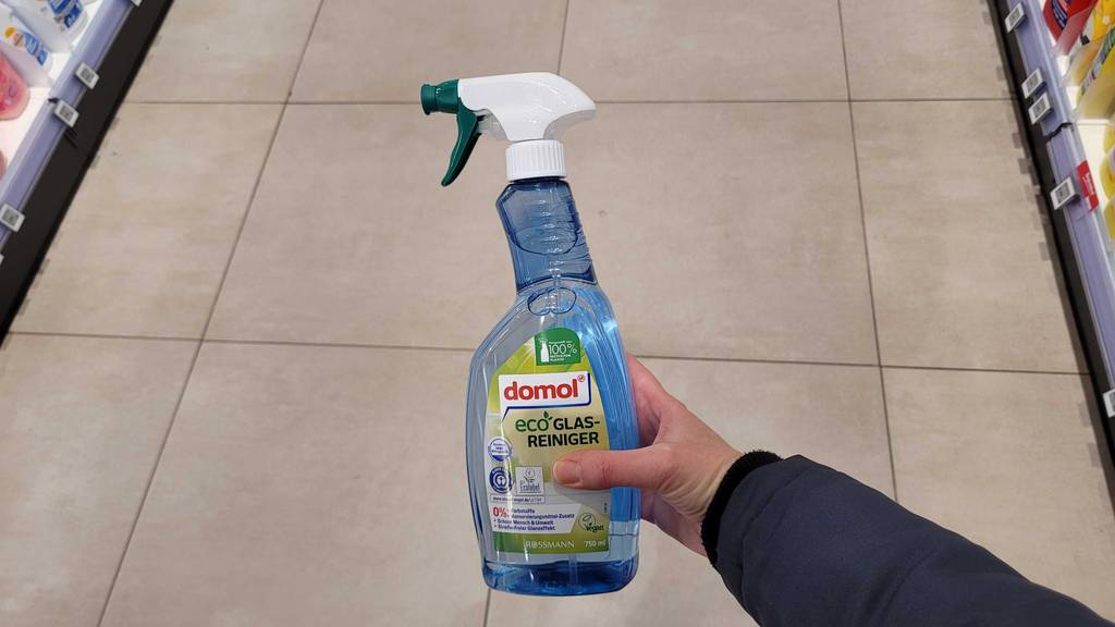 Eine Hand hält einen getesteten Glasreiniger in der Sprühflasche vor dem Boden.