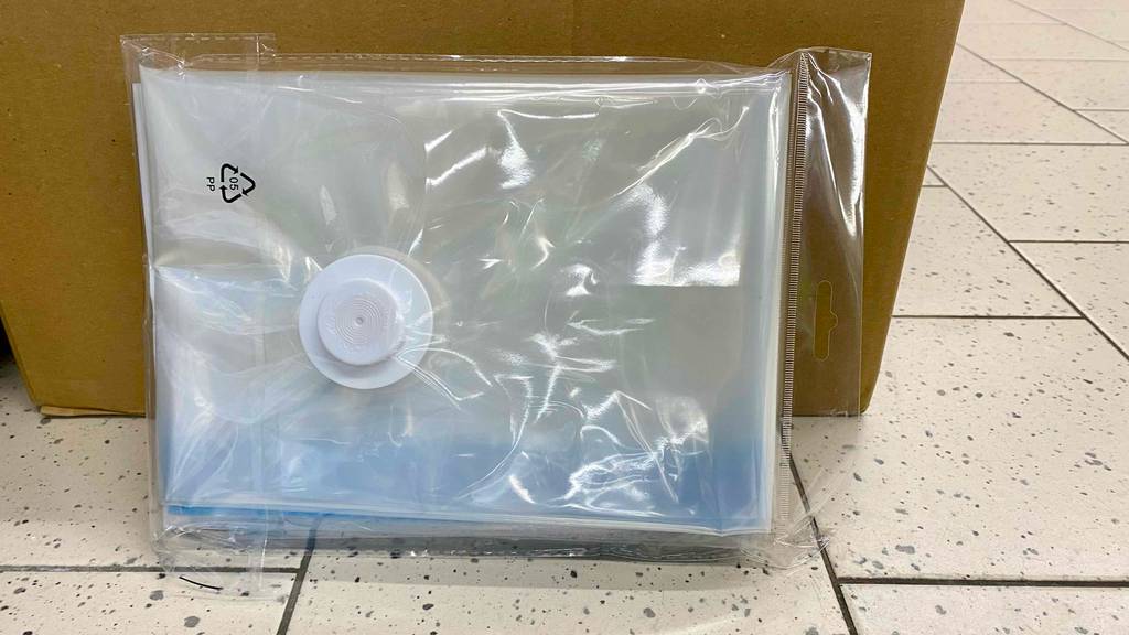 Ansicht auf den Staubsaugeranschluss eines transparenten Vakuumierbeutels im Test, der in seiner Kunststoffverpackung an einem braunen Karton lehnt.
