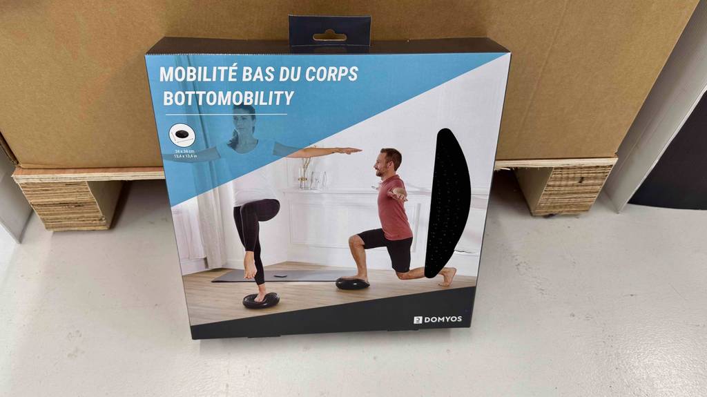 Die Verpackung eines Balancekissens im Test steht auf einem Boden vor einer Palette.