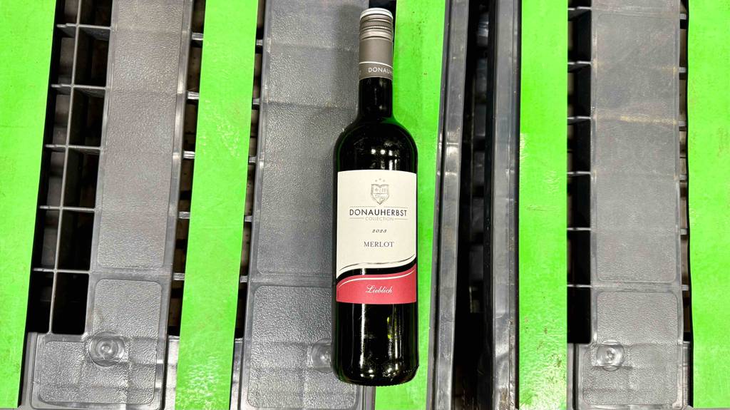 Eine Flasche getesteter Merlot liegt auf einer grüngrauen Fläche.