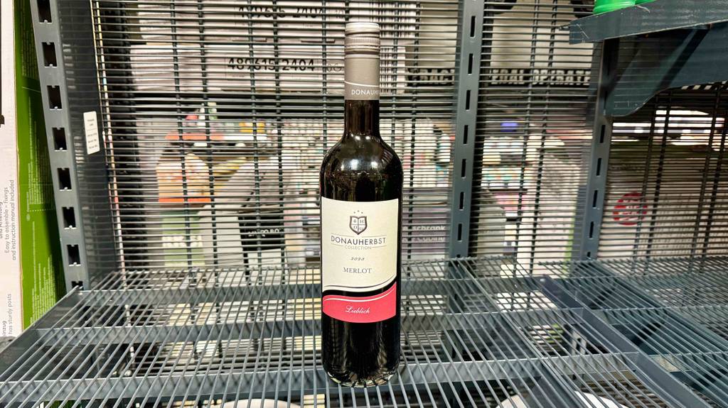 Eine Flasche Merlot steht zum testen in einem Gitterregal.
