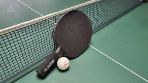 Tischtennisschläger mit Ball auf einer Tischtennisplatte vor dem Netz