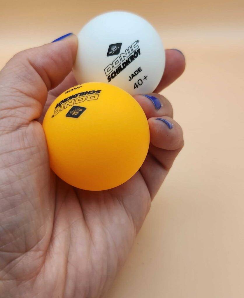 Eine Hand hält einen gelben und einen weißen Tischtennisball von Tischtennisschlägern im Test.