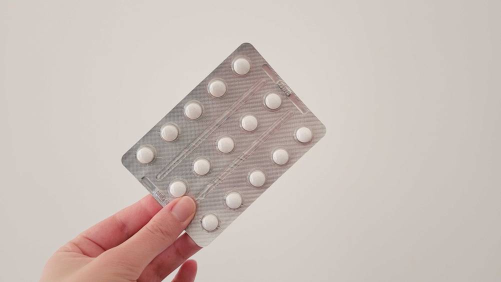Im Test: Eine Hand hält einen Tablettenblister des Vitamin K2 vor eine helle Wand.