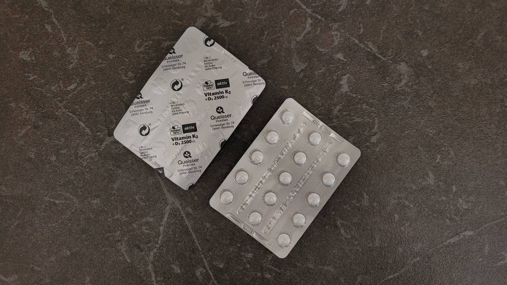 Vitamin K2 getestet: Zwei Tablettenblister einer von vorne einer von hinten auf einer dunklen Oberfläche.