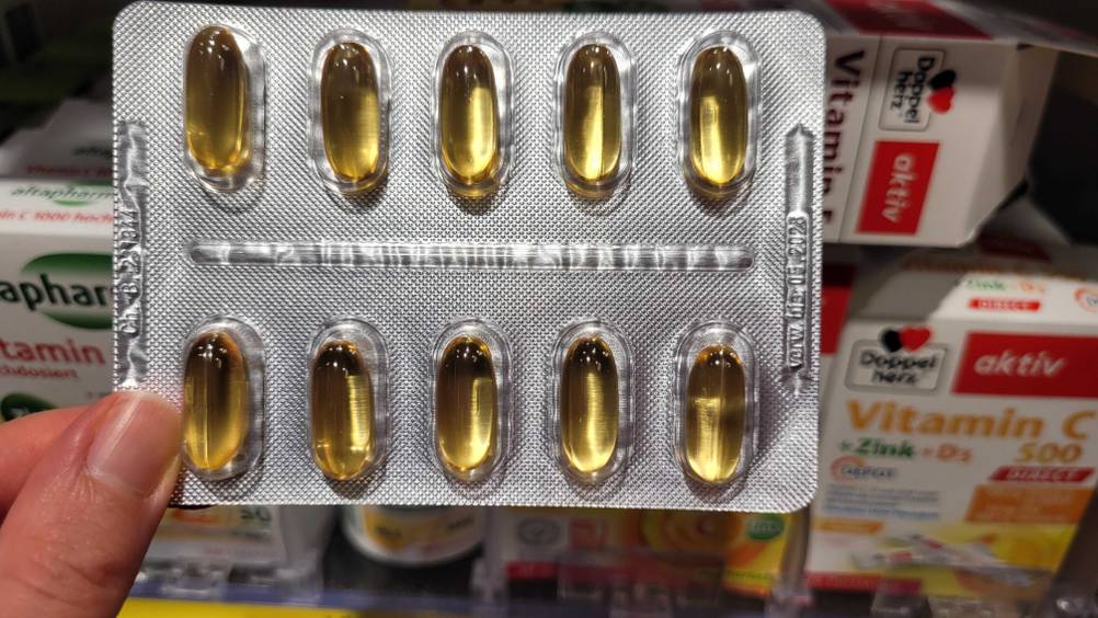 Getestet: Eine Hand hält einen Tablettenblister Vitamin E vor ein Verkaufsregal.