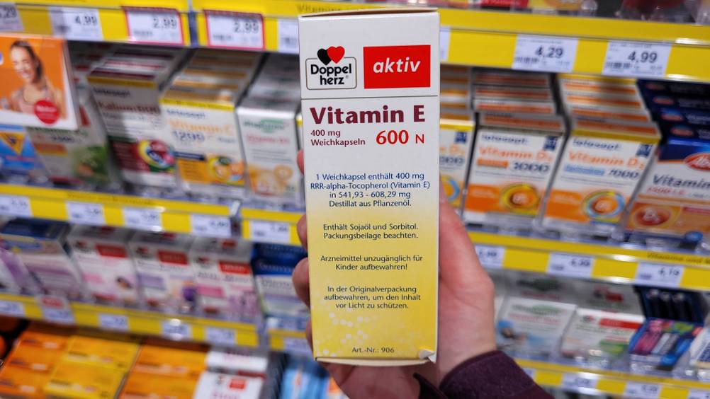 Vitamin E-Test: Eine Hand hält die Seite einer Packung vor ein Verkaufsregal.