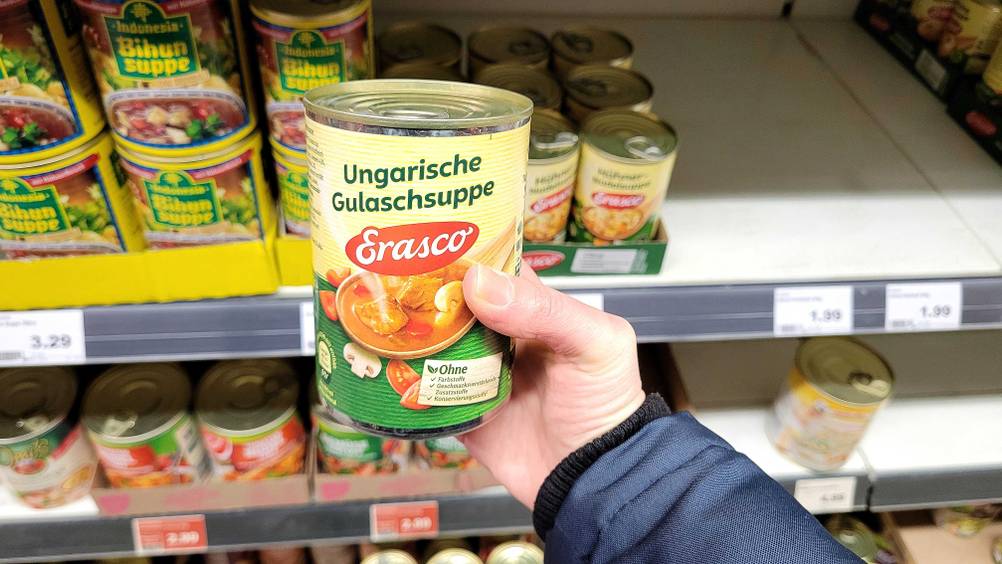 Eine Hand hält das Dosengulasch im Test vor ein Regal.