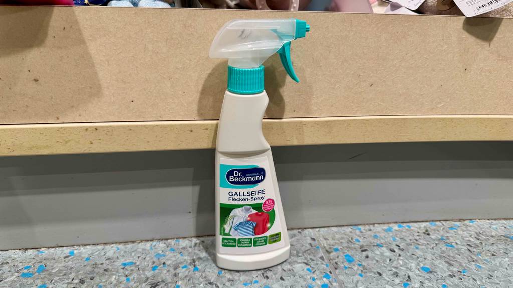 Testen: Fleckenspray in der Sprühflasche steht auf dem Boden vor einem Regal.