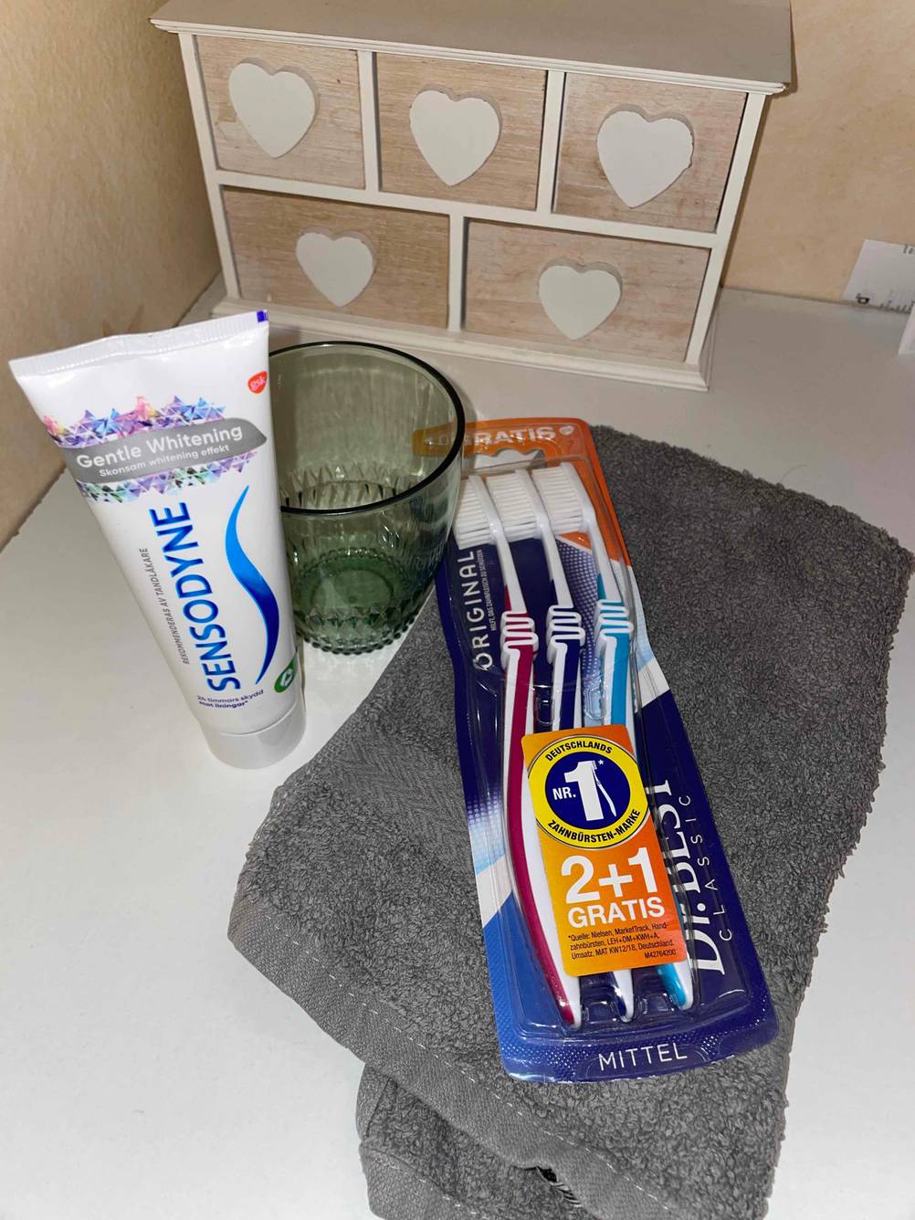 Dr. Best Zahnbürsten in Originalverpackung mit Handtuch, Zahnpasta und Zahnbecher.