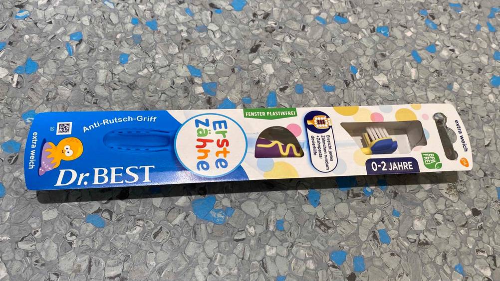 Baby-Zahnbürste im Test: ein verpacktes Modell von Dr. Best liegt auf einem gesprenkelten Boden.