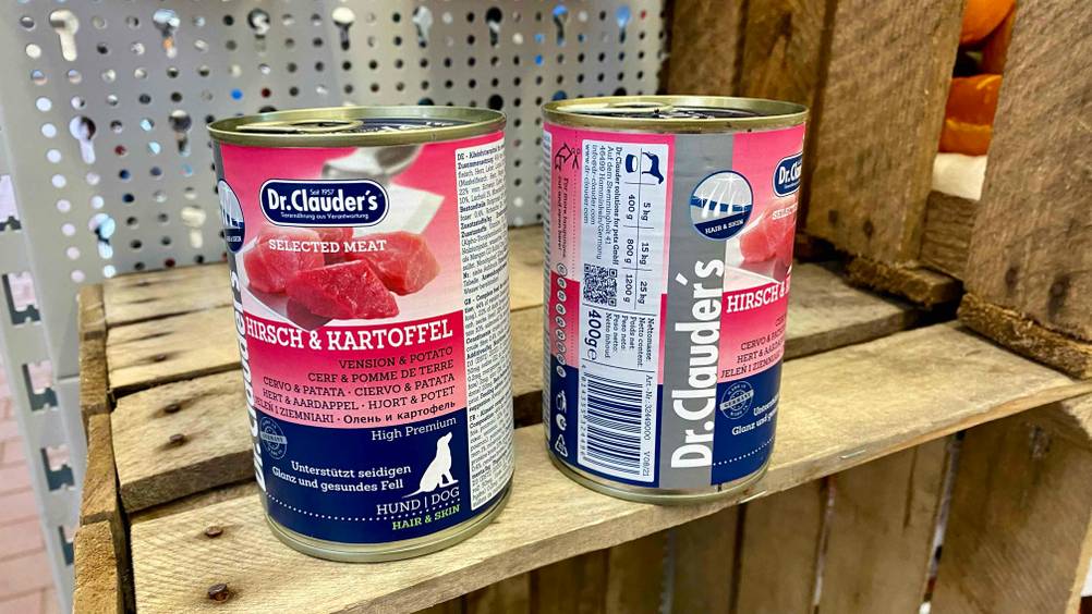 Zwei Dosen Nassfutter für den Hund stehen zum testen auf einer Holzkiste, eine davon mit Ansicht der Seite mit Fütterungsempfehlung.
