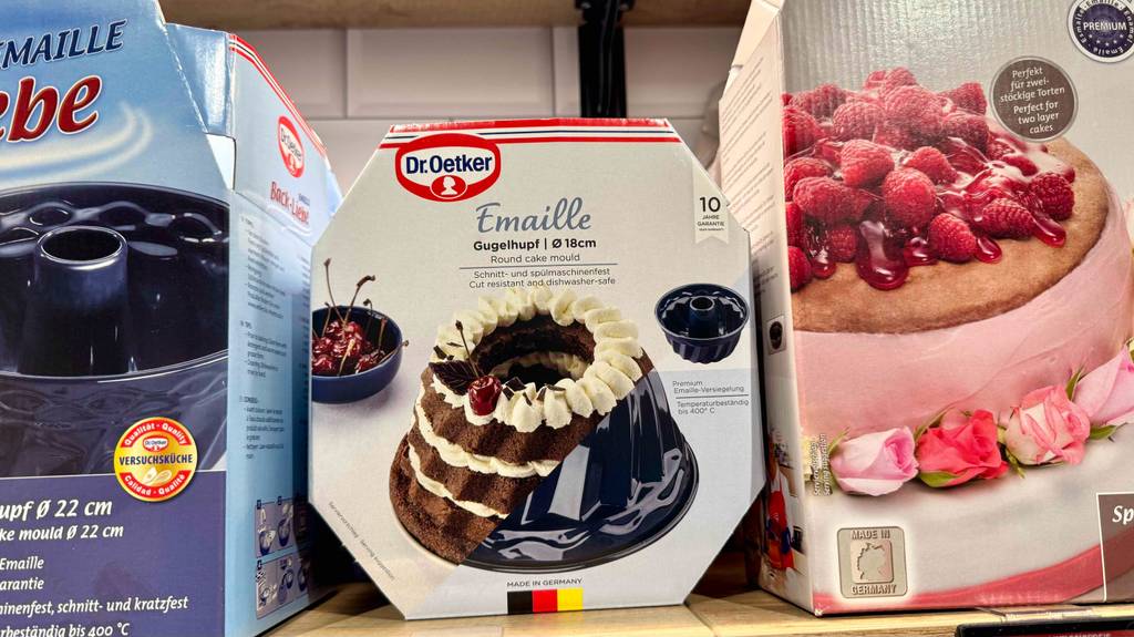 Die Backform aus Emaille im Test steht innerhalb einer Verpackung von Dr. Oetker auf einem Regal mit weiteren Backformen.