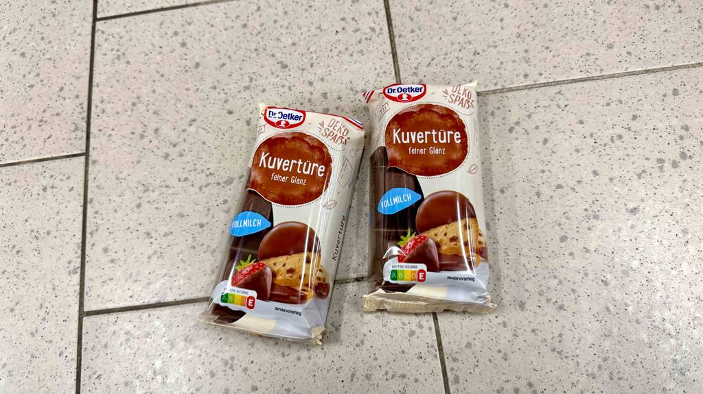 Zwei Packungen mit getesteter Kuvertüre von Dr. Oetker liegen auf einem Fliesenboden.