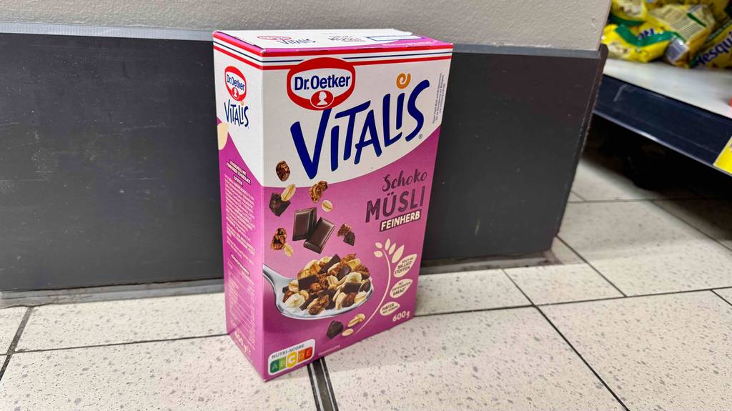 Dr.-Oetker-Vitalis-Müsli im Test: Eine 600-g-Packung mit Produktangaben steht auf dem Boden vor einem Regal.