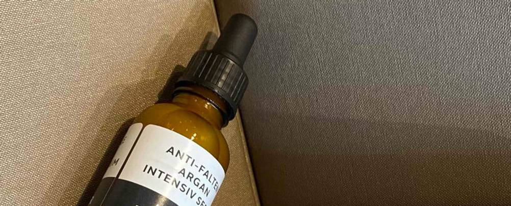 Eine Pipettenflasche mit getestetem Anti-Falten-Serum vor beigefarbenem Hintergrund.