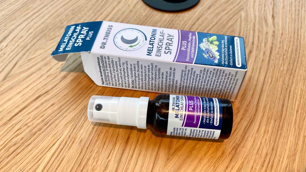 Im Test: Eine Flasche Melatonin-Spray liegt vor der Originalverpackung horizontal auf einer Holzfläche.