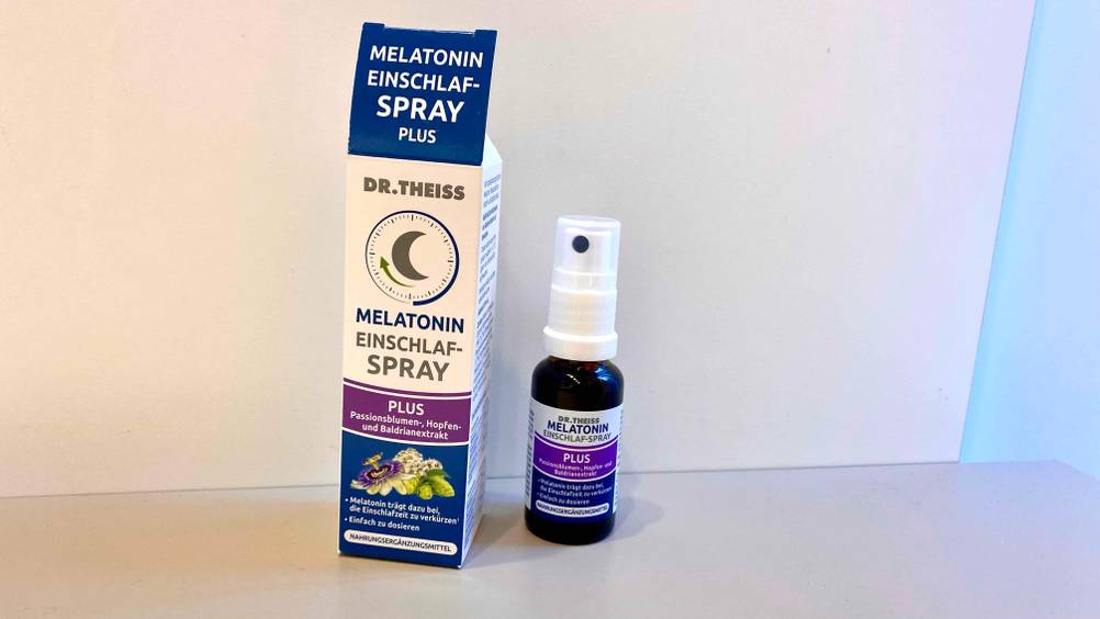 Eine Flasche Melatonin-Spray im Test neben der Originalverpackung vor einer hellen Wand stehend.