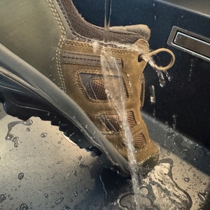 Wasser perlt trotz starkem Wasserstrahl von einem Schuh im Waschbecken ab