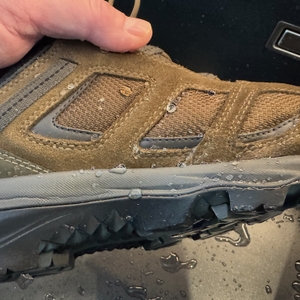 Hand hält einen Schuh in einem Waschbecken, leichte Tropfen sind außen zu sehen