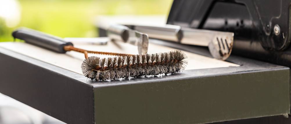 Grillbürste und Grillzange liegen auf der Ablage eines Grills.