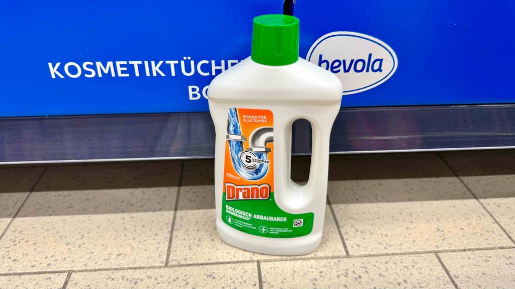 Getestet: Abflussreiniger in der weißen Flasche aus Kunststoff steht vor einem Regal auf dem Boden.