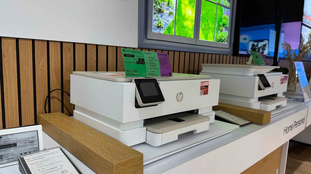Ein Drucker bis 150 Euro im Test von schräg seitlich neben anderen Produkten in einem Verkaufsraum.