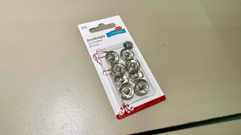 Auf einer hellen Fläche liegt eine Packung der getesteten Druckknöpfe.