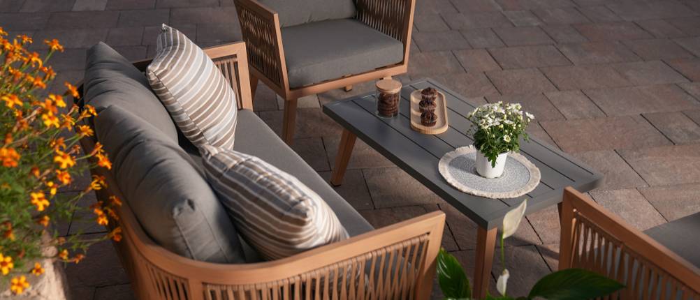 Sitzecke mit einer Holzbank und zwei Holzstühlen samt dunklen Sitzpolstern auf einer Terrasse