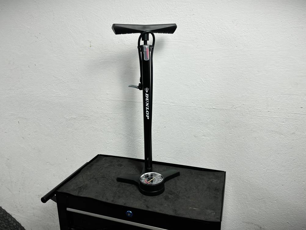 Die Dunlop 17049 Standpumpe steht auf einer Werkbank vor einer weißen Wand. Der Pumpenzylinder ist senkrecht montiert.
