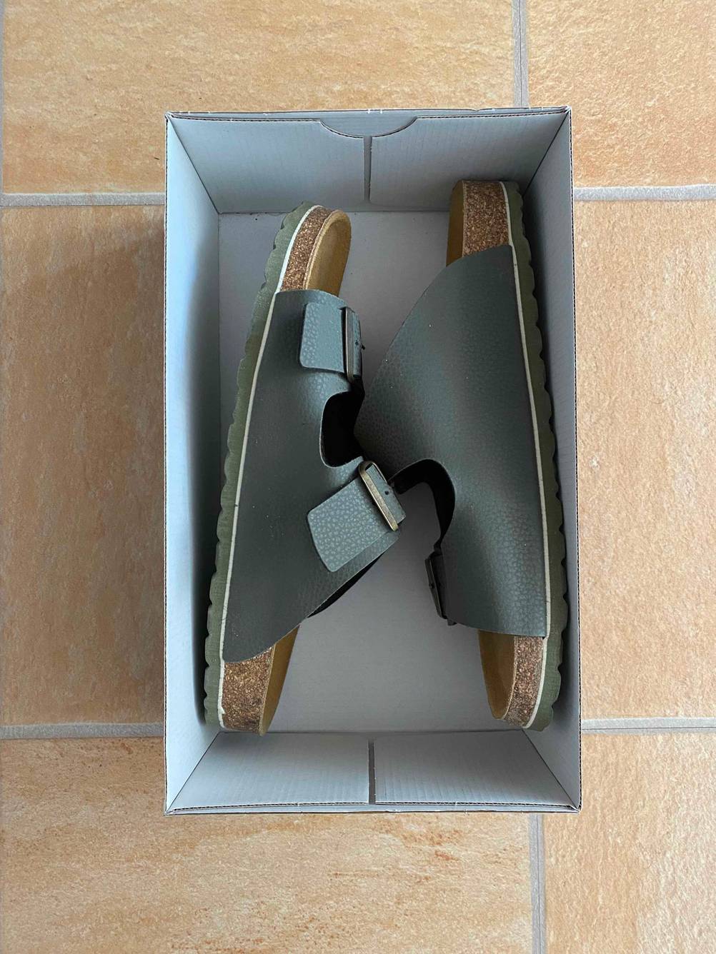 Hausschuhe für Herren im Test: Ein Paar liegt in der Seitenansicht in einem Schuhkarton.