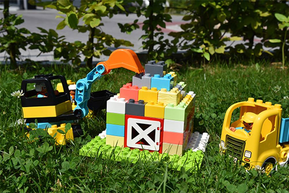 Duplo im Test: Ein Duplo Bagger und LKW sowie ein selbst gebautes Haus auf einer Wiese.