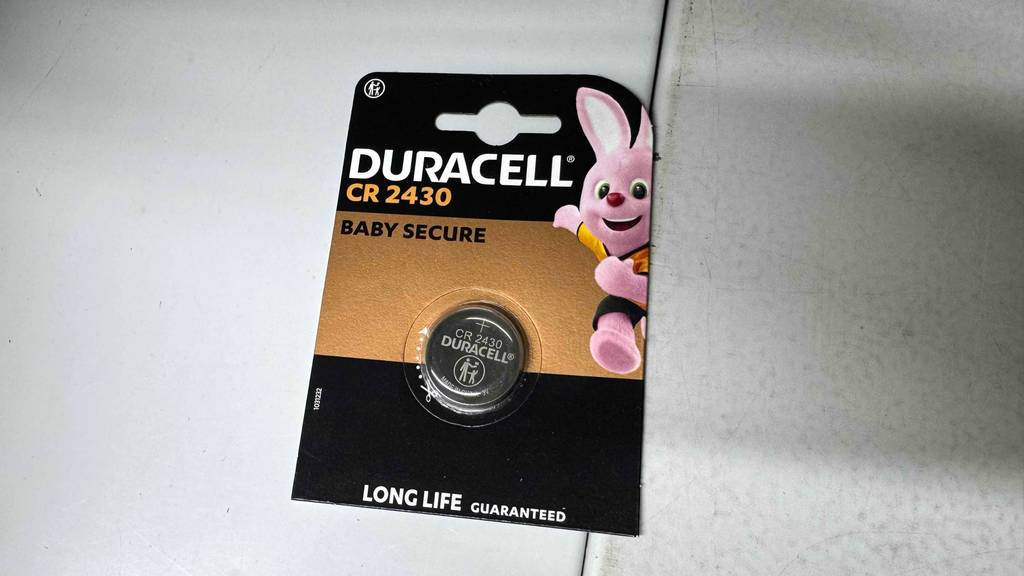 Eine Packung mit einer getesteten CR2430 Knopfbatterie liegt auf einer weißen Oberfläche.