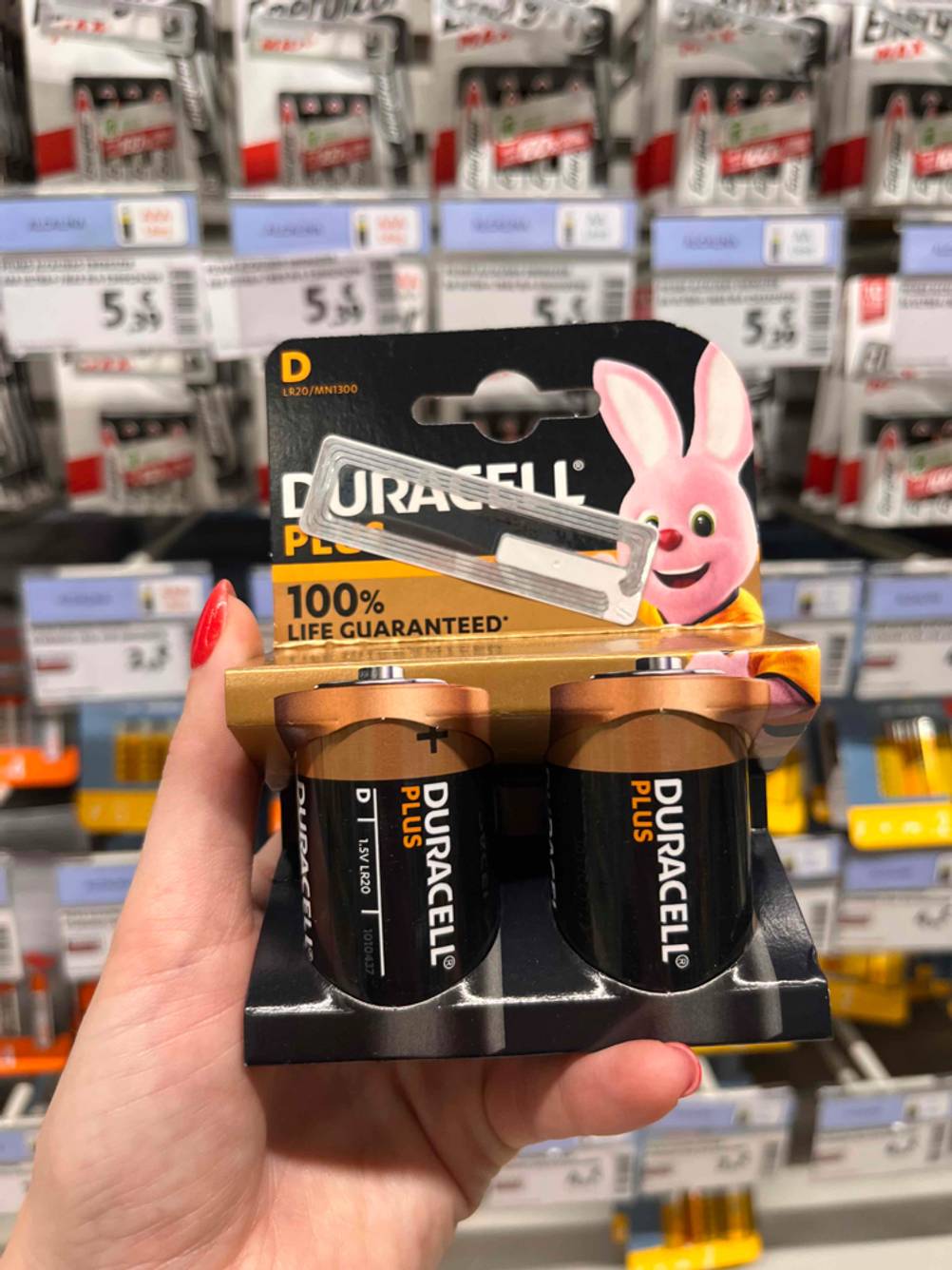 Hand hält D-Batterien im Test der Marke Duracell in der Originalverpackung vor ein Verkaufsregal.