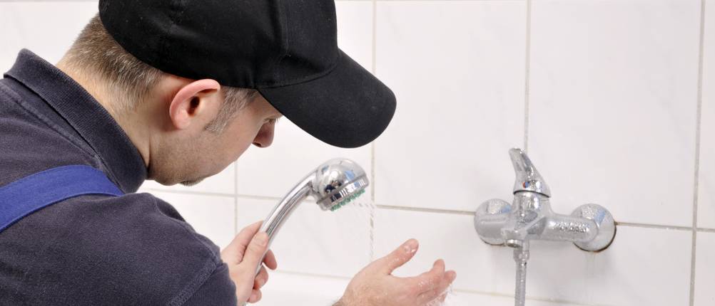 Durchlauferhitzer mit Fernbedienung Test: Ein Mann in Monteurkleidung fühlt mit der Hand die Wassertemperatur an einer Badewannenarmatur in einem weißen Bad.