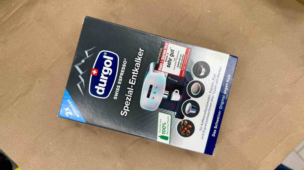Im Test: Ein Entkalker für Kaffeevollautomaten in der Packung mit zwei Entkalker-Flaschen liegt auf einer braunen Pappe.
