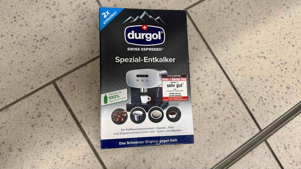 Der getestete Entkalker für Kaffeevollautomaten in der Packung mit zwei Entkalker-Flaschen liegt auf dem Boden.