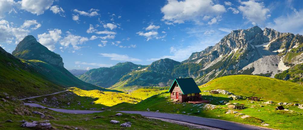 Landschaftsbild mit Bergen im Hintergrund, einer Straße und einer kleinen Hütte im Durmitor-Nationalpark.