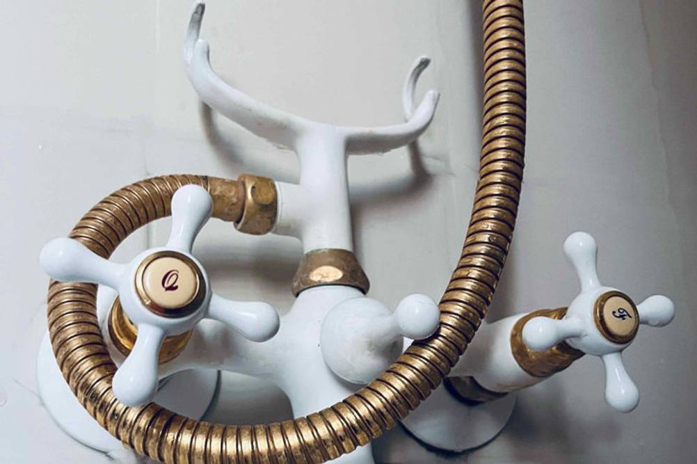 Duscharmatur in Weiß und Gold im Test: Armatur ist an einer hellen Wand angebracht.