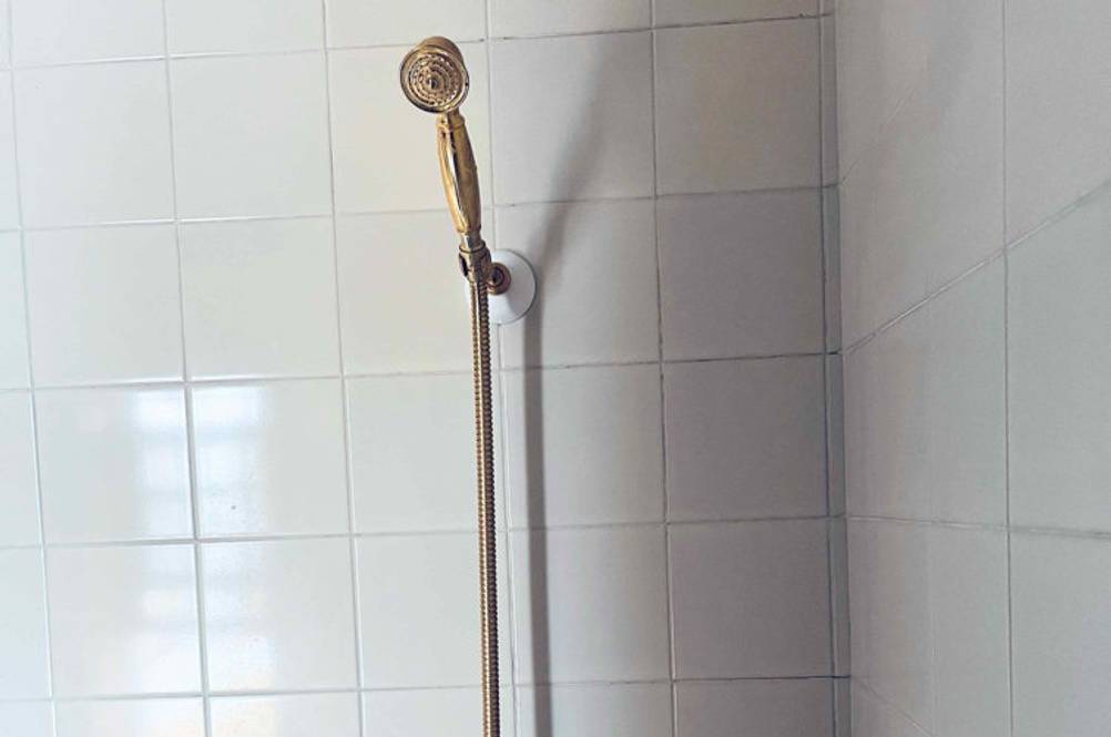 Getestete Duscharmatur in Weiß und Gold ist an einer hellen Fliesenwand befestigt.