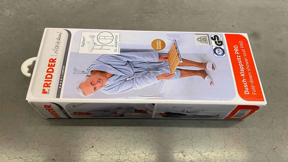 Getestet: Eine Verpackung eines Duschklappsitzes horizontal auf einem Betonboden.