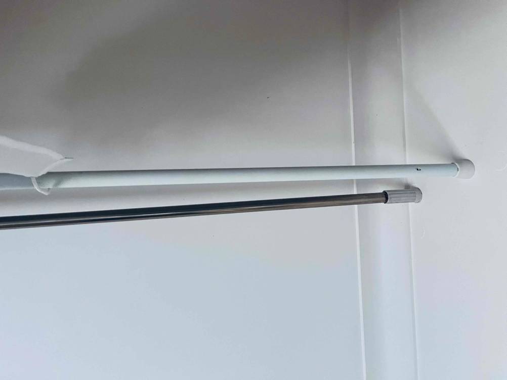 Nahaufnahme zweier getesteter Duschstangen in Weiß und Grau mit schraubloser Befestigung an einer weißen Wand.