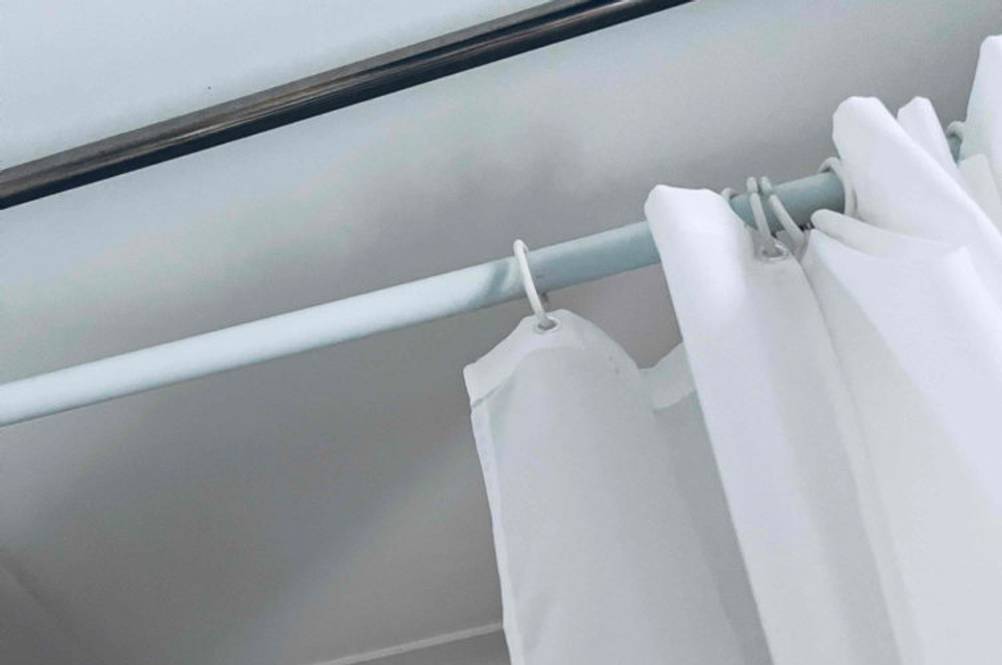 Weiße, verstellbare Duschstange im Test mit weißem Duschvorhang im Badezimmer.