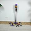 Der Dyson V15 Detect mit aufgestecktem Rohr und allen Zubehörteilen auf dem Boden verteilt. Das Gerät steht senkrecht an der Wand.