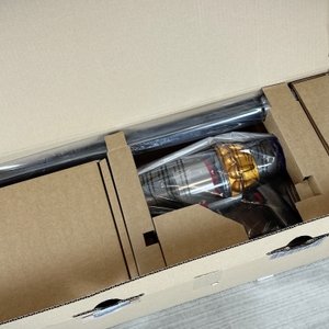 Zu sehen ist der geöffnete Versandkarton des Dyson V15 Detect. Das Gerät und das Zubehör sind einzeln in Kartonfächern verpackt.