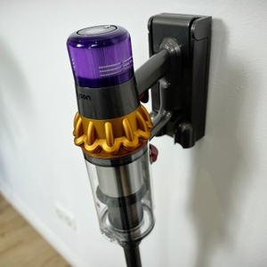 Der Dyson V15 Detect ist in die Wandhalterung eingesteckt. Das Gerät hängt senkrecht an der Wand und ist vollständig geladen.