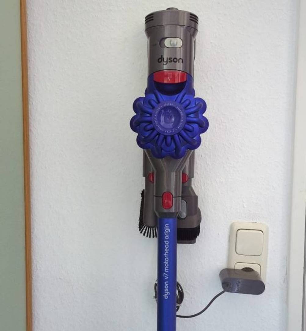 Dyson Tierhaarstaubsauger im Test: ein violettfarbenes Modell inklusive verschiedener Bürstenaufsätze hängt in der Ladestation an einer weißen Wand.